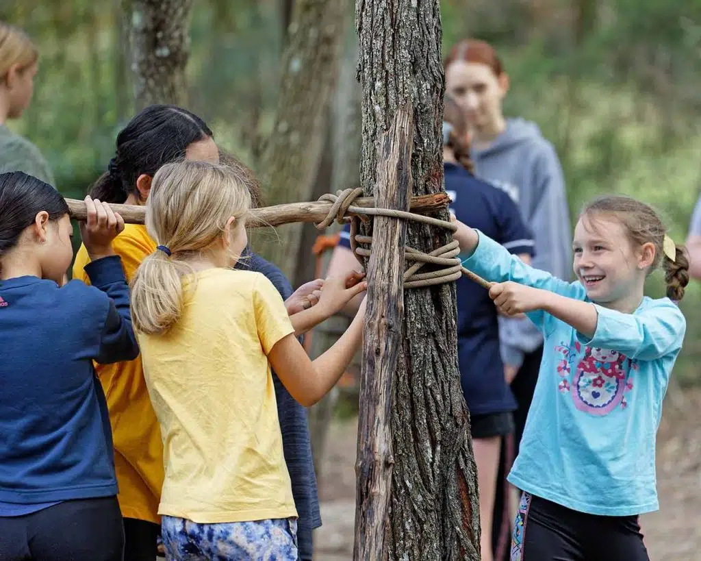 Children tying knots around a tree whilst a PGL instructor looks on and supervises.