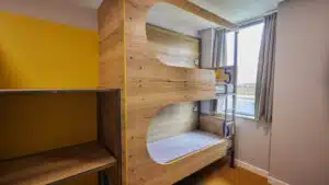 A room with two wooden bunk beds near a window with grey curtains, numbered “5” on each bunk. The room at PGL Centres features a yellow accent wall and beige flooring.