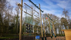 A high ropes course at one of the PGL Centres in a forested area offers various challenges, including tires, ropes, and a climbing net against a clear blue sky.