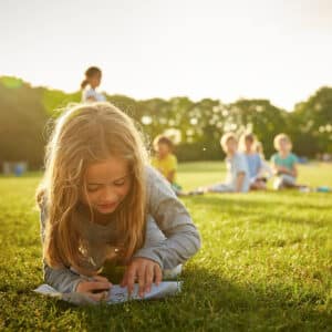 A student drawing on the grass with a group of kids in the background