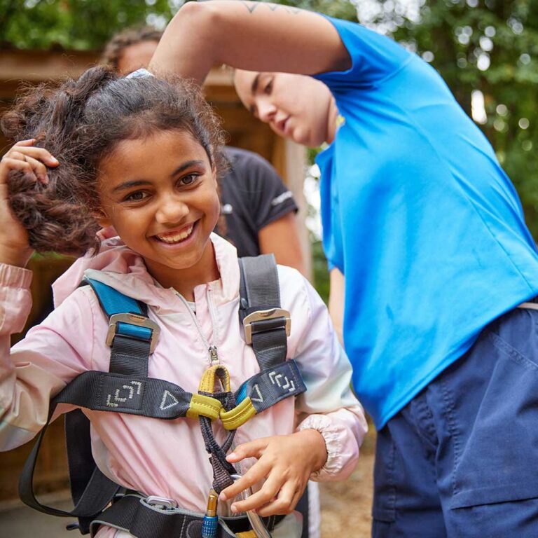PGL Instructor prepping a child for a climbing session with a harness and carabiner
