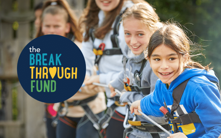 A group of children in harnesses smiling and pulling on a rope outdoors with "the Breakthrough Fund" logo to the left.