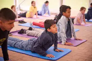 Children practicing yoga on mats in an outdoor setting, seamlessly integrating it into a multi-activity routine, performing the cobra pose.