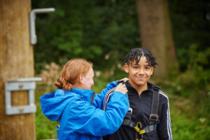 A woman in a blue jacket assists a person in a harness outdoors, embodying principles of how to promote physical activity in schools through engaging and dynamic experiences.