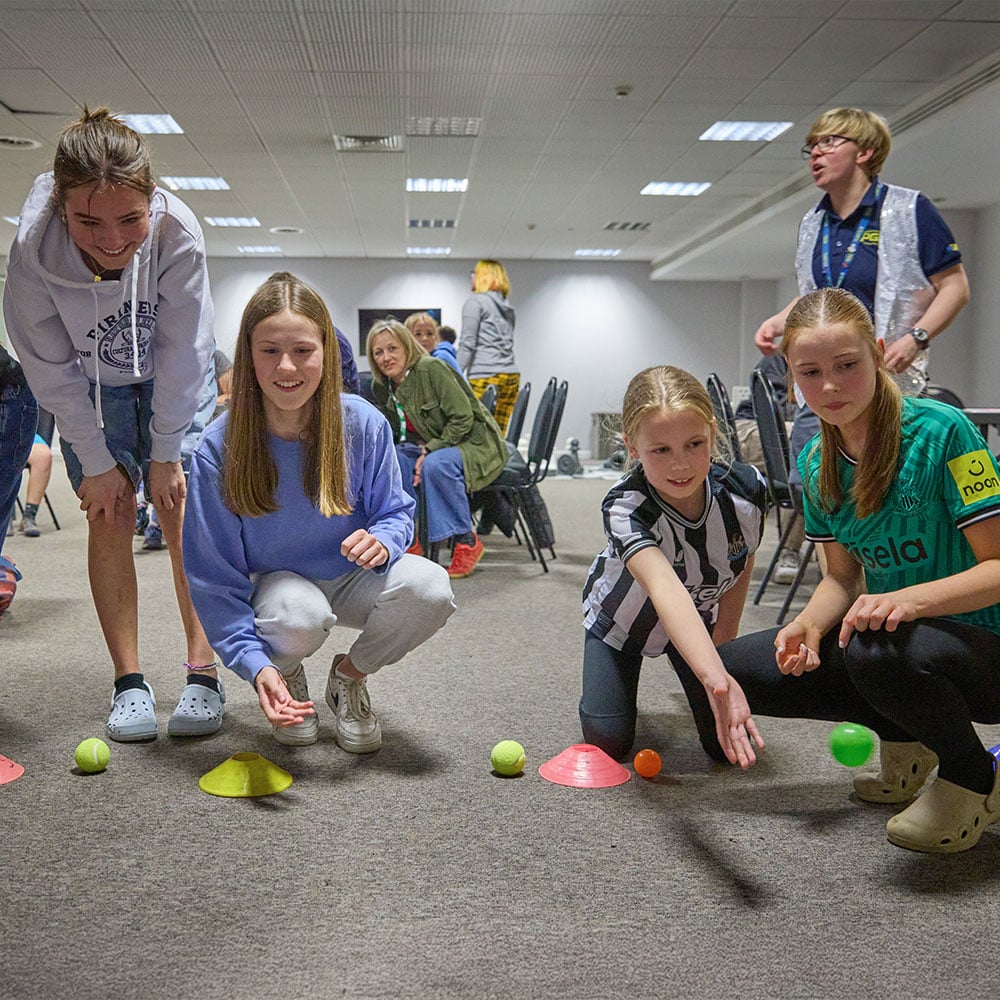 Children and adults are playing a game indoors with tennis balls and colored cones, focusing on coordination and teamwork.