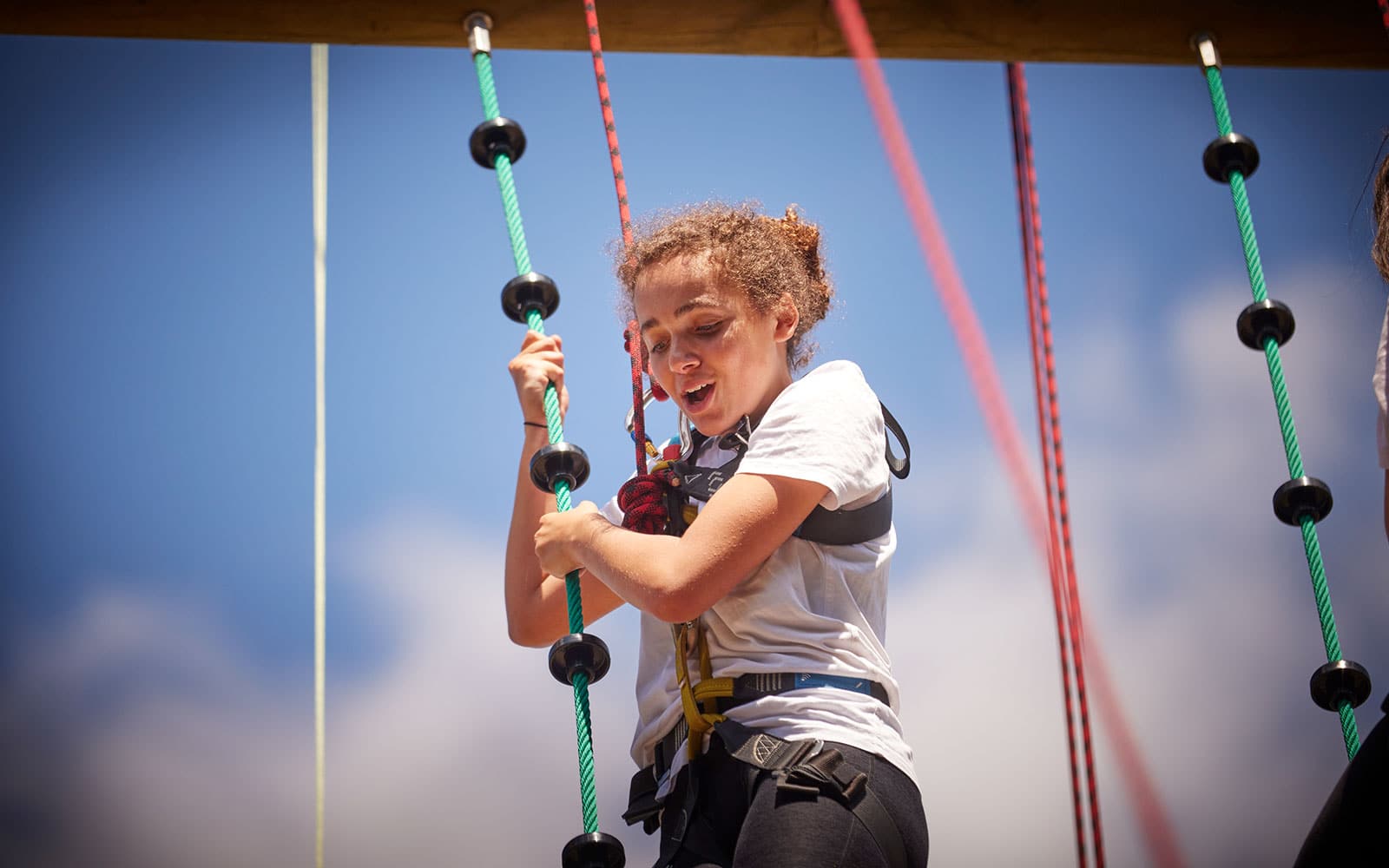 Person climbing a rope ladder outdoors under a clear blue sky.