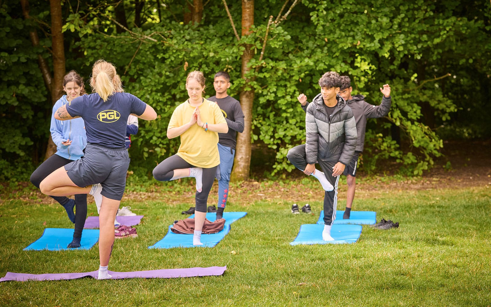 Group of people practicing yoga on mats outdoors with an instructor guiding them.