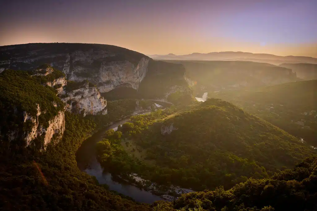 A winding river flows through a lush green valley surrounded by rocky hills and cliffs at sunset, creating the perfect backdrop for a multi-activity adventure.