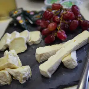 Assorted soft cheeses and a bunch of red grapes arranged on a dark serving board, perfect for a multi-activity gathering.
