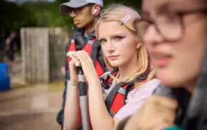 Three young people in life jackets enjoy a multi-activity adventure outdoors, with one person in focus holding a paddle and looking at the camera while the others are out of focus.