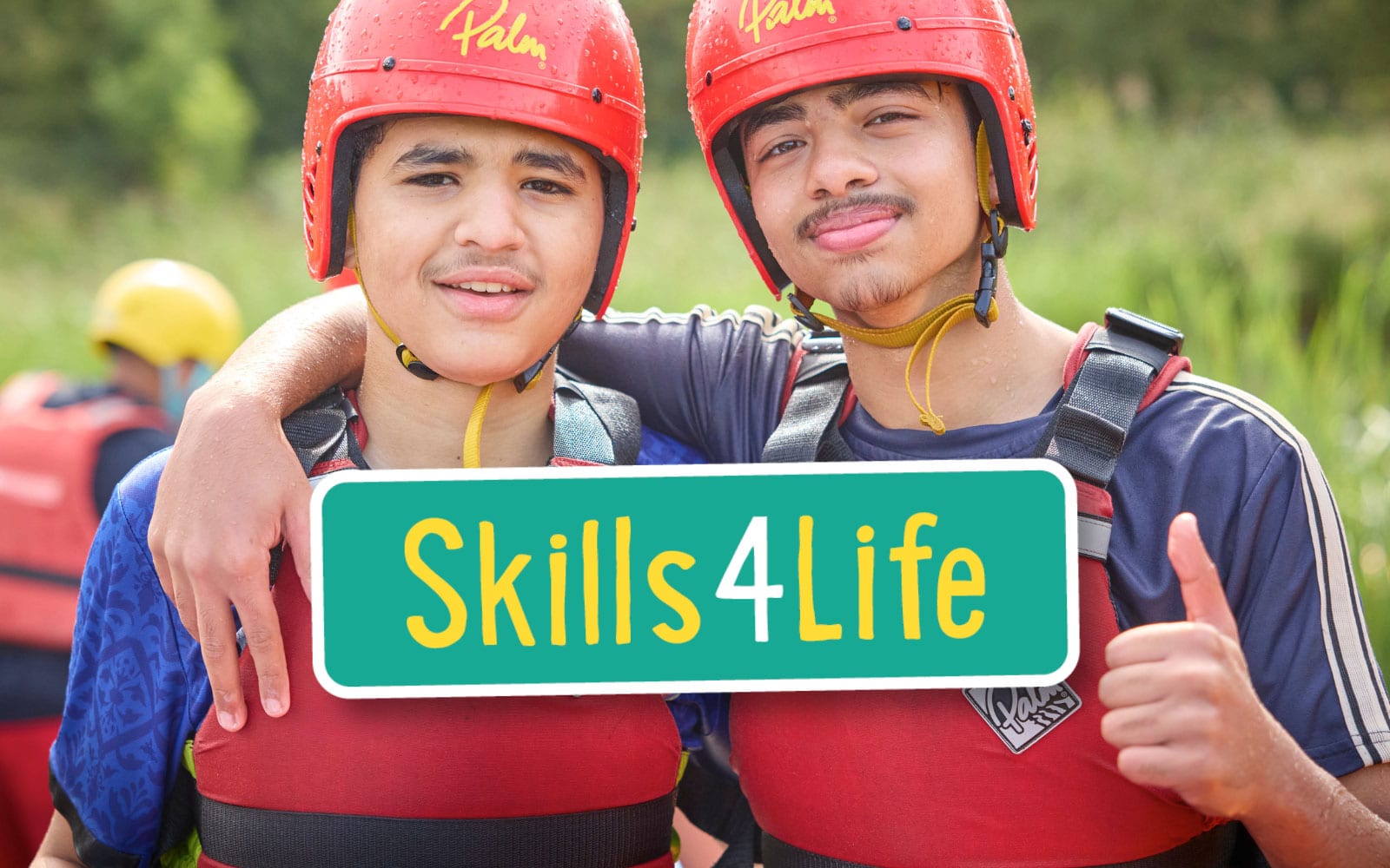 Two young people wearing red helmets and life vests stand side by side, smiling at the camera, with the “Skills4Life” sign in front of them—ready for a day of multi-activity adventures.