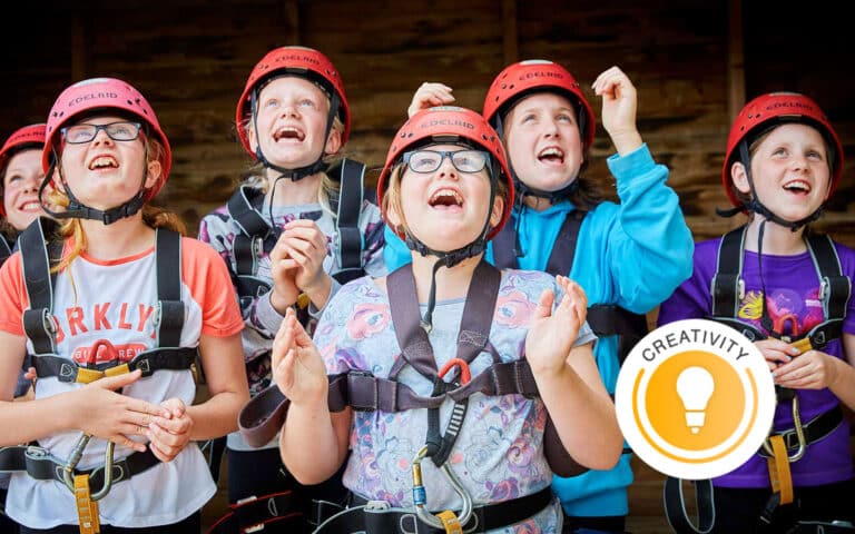 A group of children wearing helmets and harnesses look up excitedly, standing together and smiling. A "Creativity" badge with a lightbulb icon is overlaid on the image.