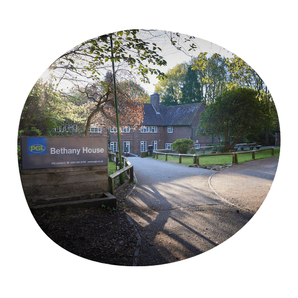 A large brick building called Bethany House is surrounded by trees and greenery, with a sign and driveway visible in the foreground.