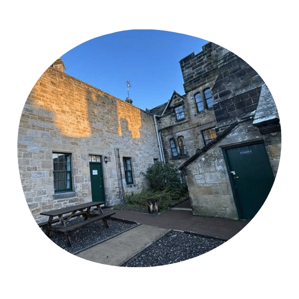 A courtyard with stone buildings, green doors, a picnic table, and clear blue sky overhead.