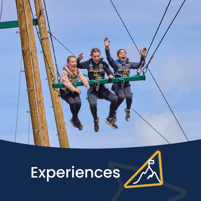 Three people are seated and harnessed on a high swing ride, suspended in the air, appearing excited. The word "Experiences" and a mountain icon are shown below them.