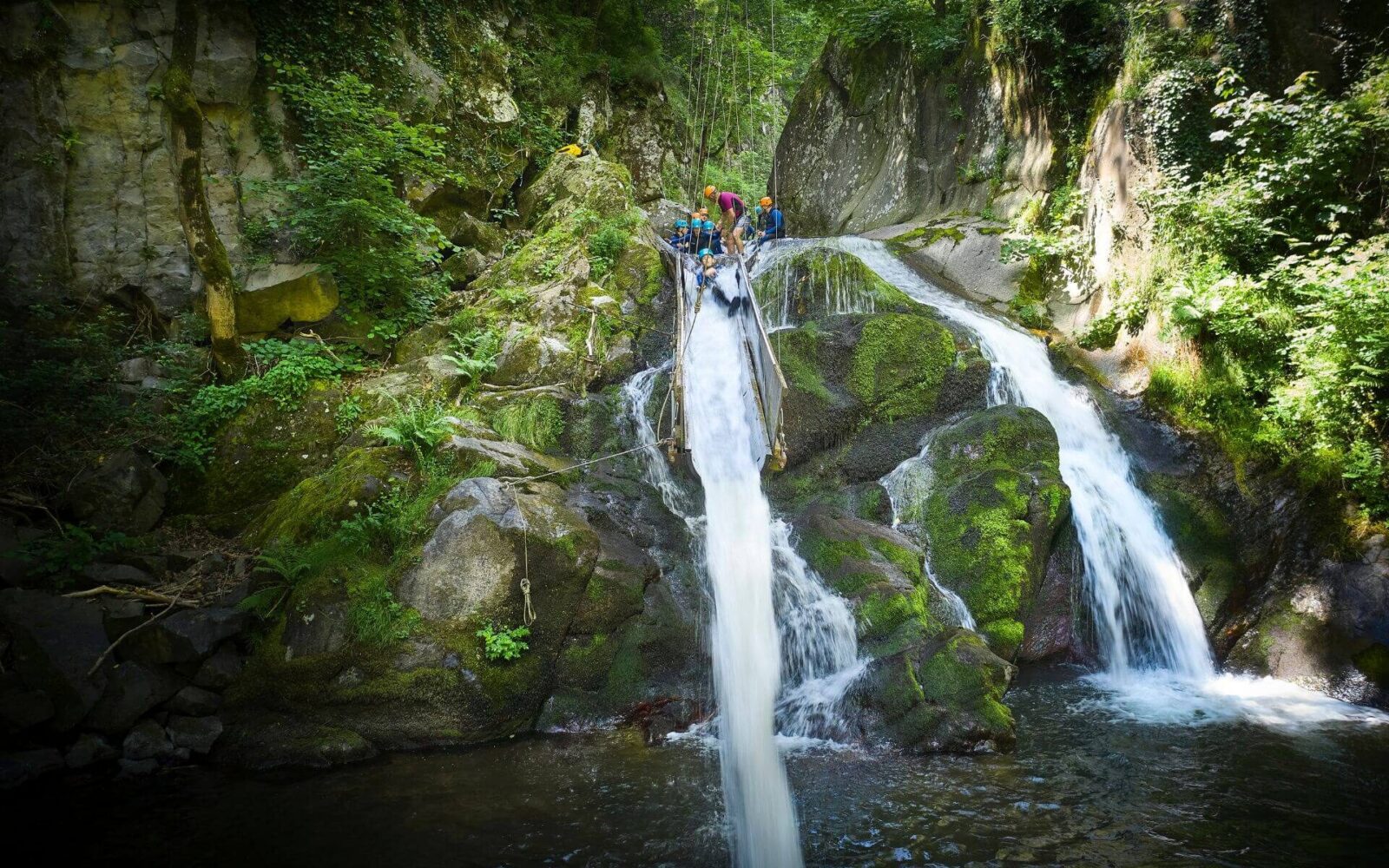 Children in helmets sliding down a natural rock waterfall during an activity in the Ardèche Gorge on a PGL school trip to France.