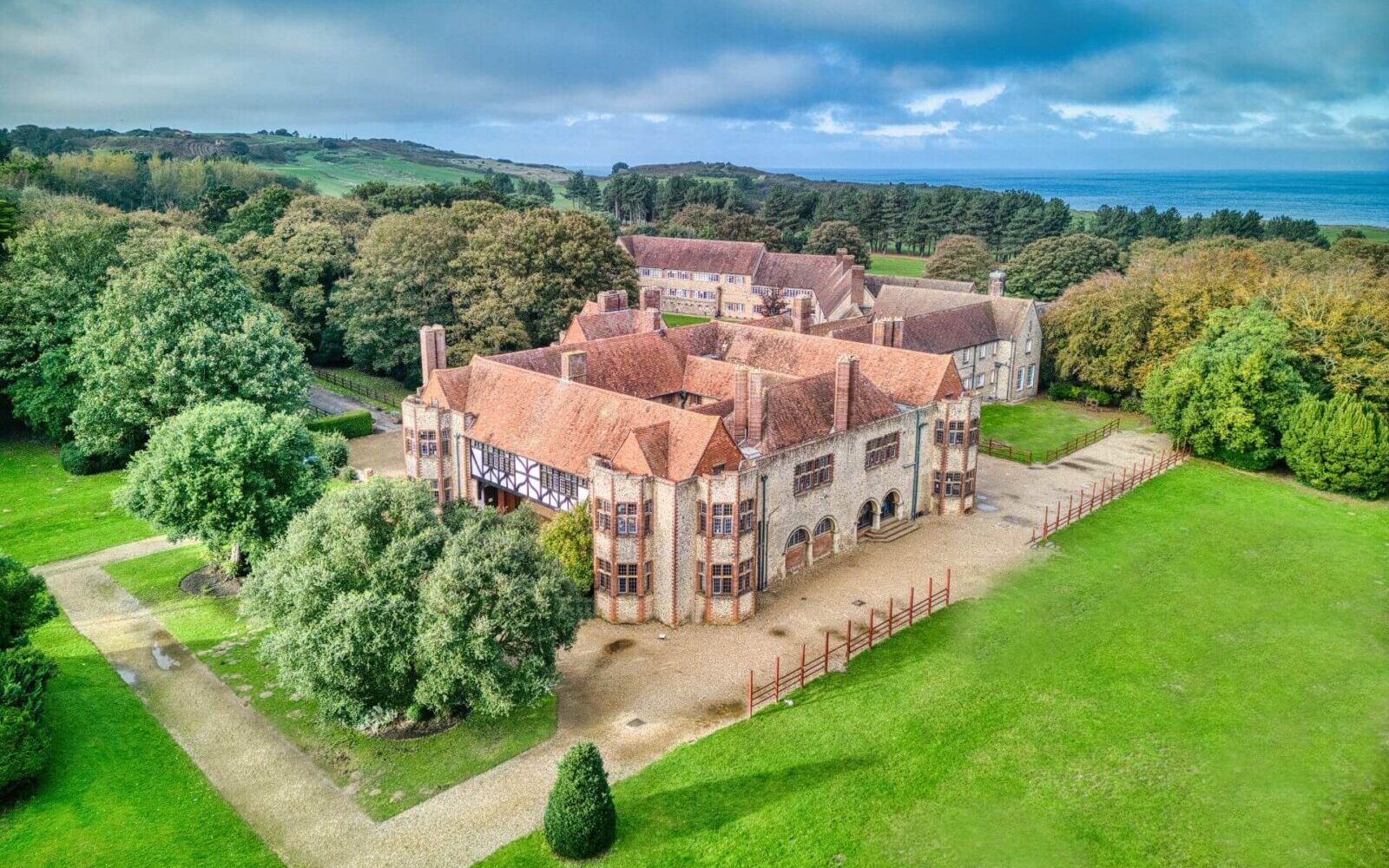 Aerial view of Overstrand Hall, a historic manor house set in expansive grounds with the North Norfolk coast visible in the background, home to a PGL school residential centre