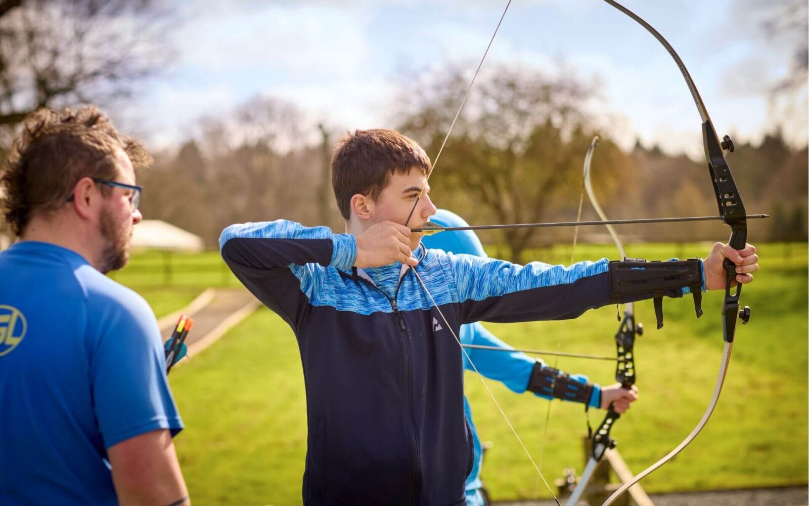 A young person taking aim with a bow and arrow during an archery activity on a PGL SEND residential trip, supervised by a PGL instructor