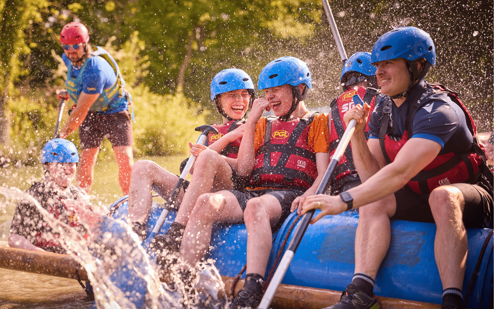 A group of people wearing helmets and life jackets are white-water rafting, laughing as water splashes around them on a sunny day.