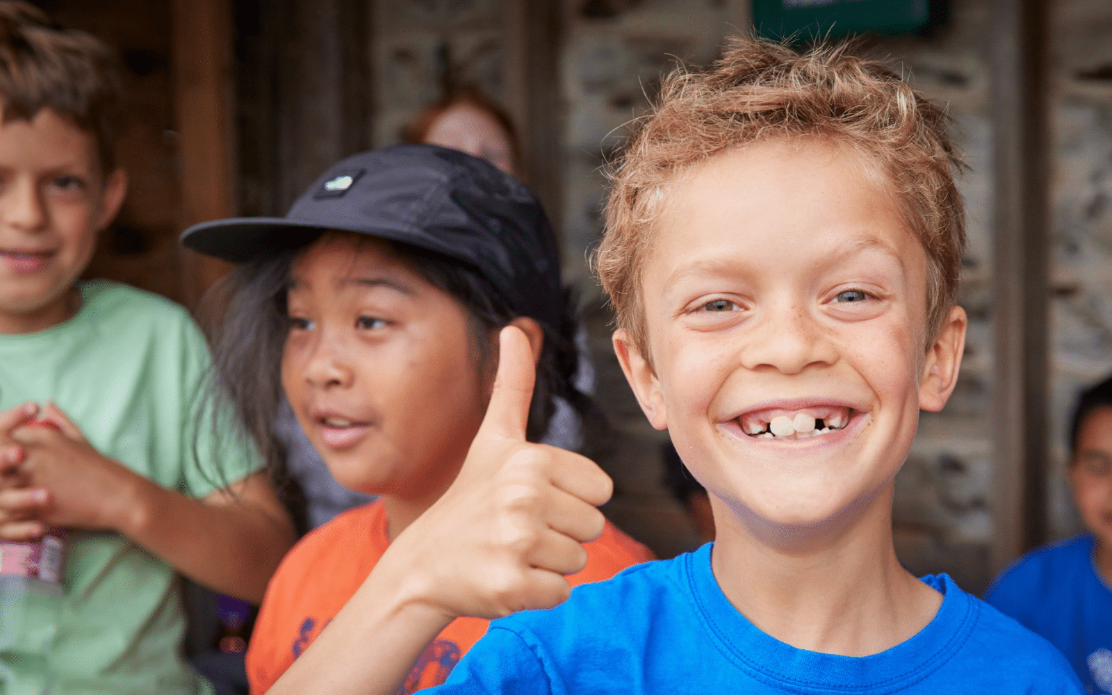 A boy with a missing tooth gives a thumbs up, looking excited for his school trip, with other children in the background.