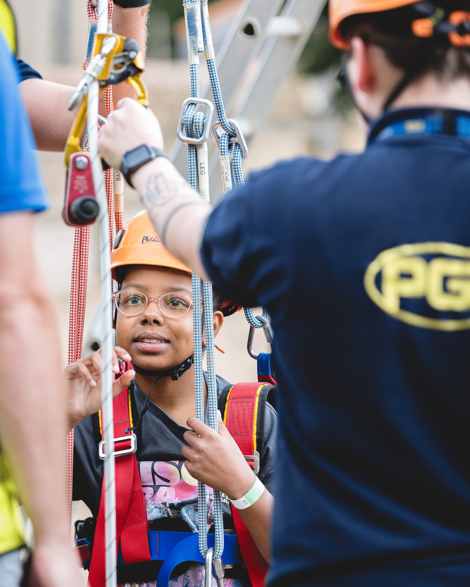A person in a climbing helmet and harness receives instruction from a staff member whilst attached to climbing ropes.